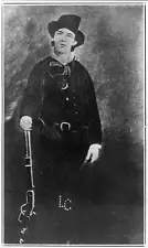 Photo:Billy the Kid, full, standing, holding carbine